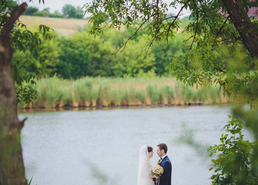 How Much Does Wedding Wire Cost for Wedding Venues? (And Is It Actually Worth It?) 2 Bride and groom standing by a lakeside during an outdoor wedding, often featured in venue listings when researching how much does wedding wire cost