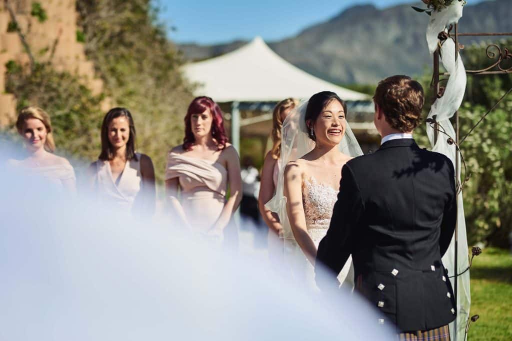 How Much Does Wedding Wire Cost for Wedding Venues? (And Is It Actually Worth It?) 3 Bride smiling during an outdoor wedding ceremony with bridesmaids in the background, similar to photos used when considering how much does wedding wire cost for venues