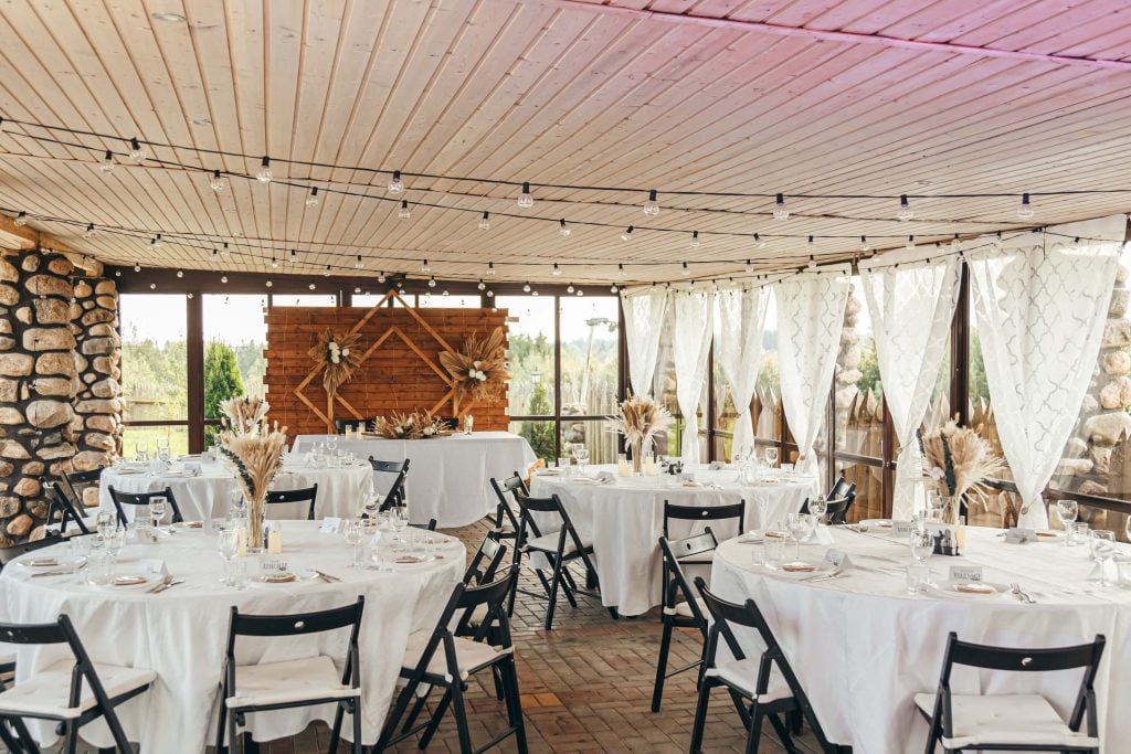 Wedding Venue Off Season Booking Strategy: Mid-Week + Shoulder-Season Plays 2 Indoor wedding reception space set with round tables, string lights, and neutral decor for shoulder-season events.
