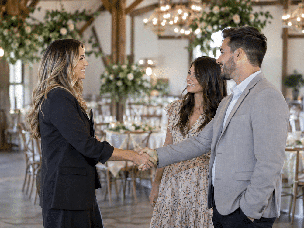 Wedding Venue Marketing Cost: What Venues Actually Spend + What Drives It 4 Wedding venue owner shaking hands with an engaged couple inside a decorated reception space after a venue tour.